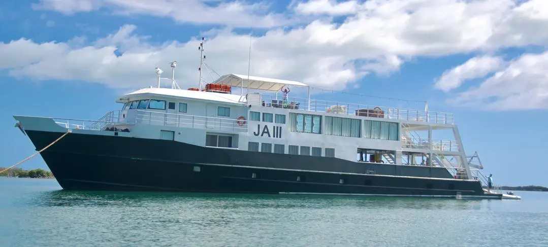 28515bd8a169c6c24446b683b1aae5f3 Large white and black boat with "JA III" on the side, anchored in calm waters under a partly cloudy sky.